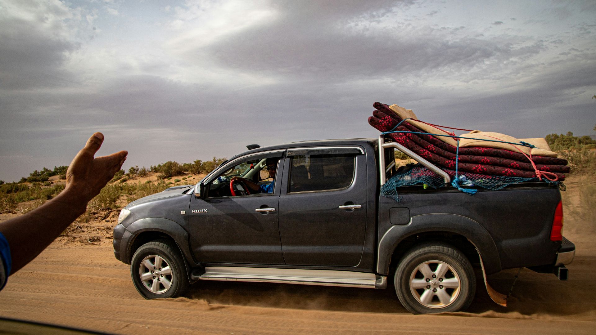 Dark pickup truck driving on a dusty desert road.