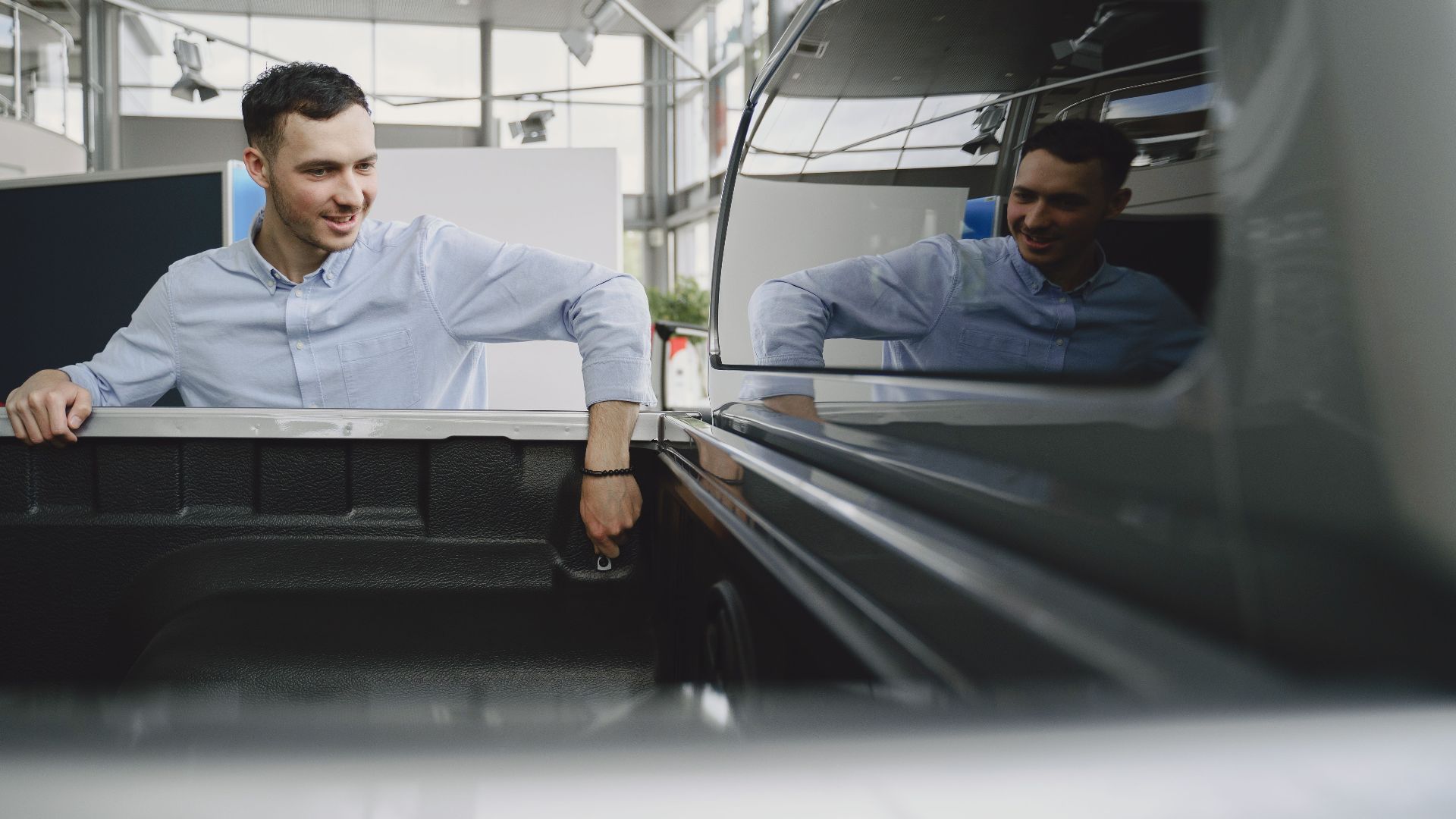 Man in a showroom examining the bed of a pickup truck, reflecting natural curiosity.