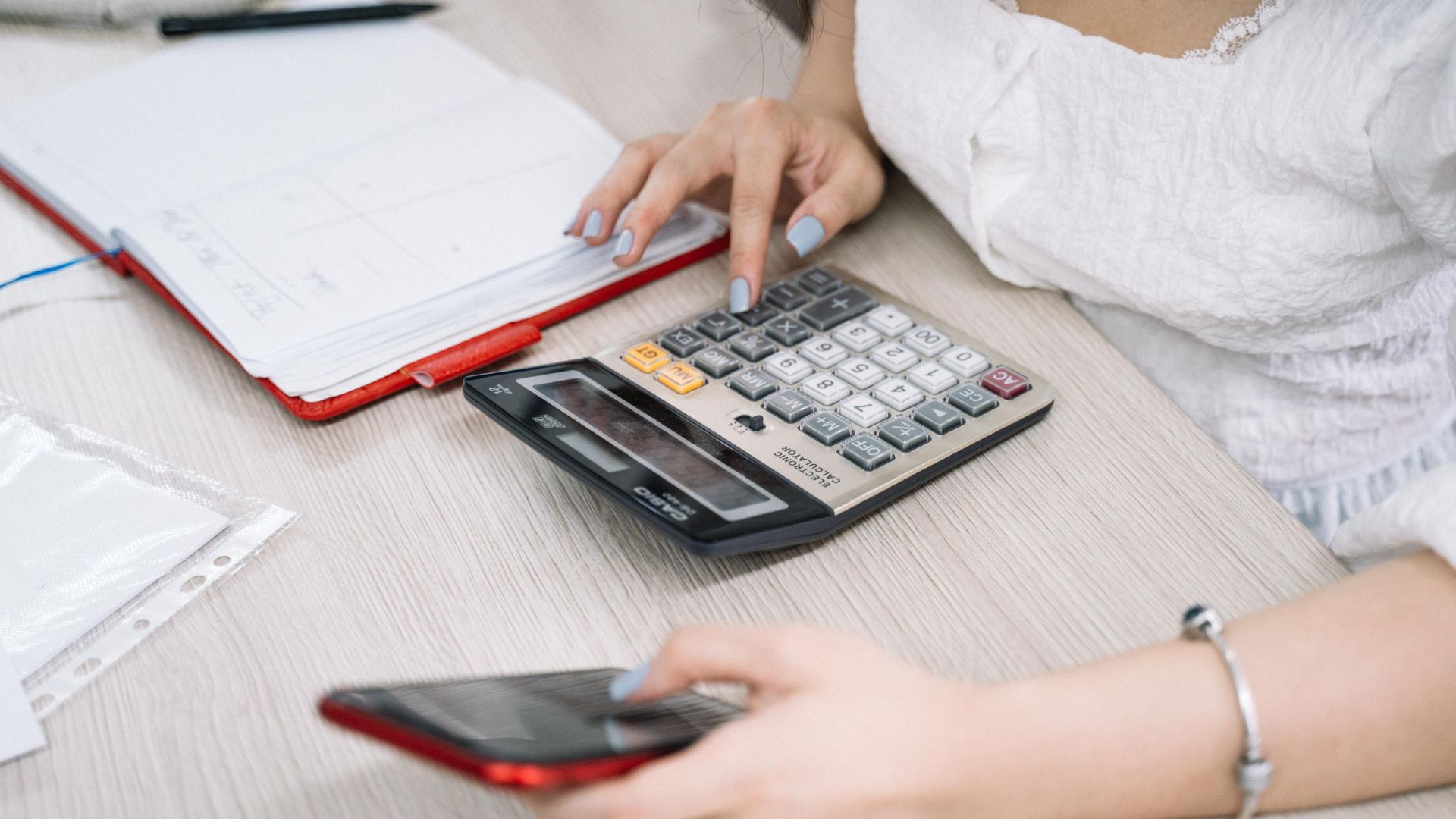 Close-up of a woman using a calculator and phone at her office desk.