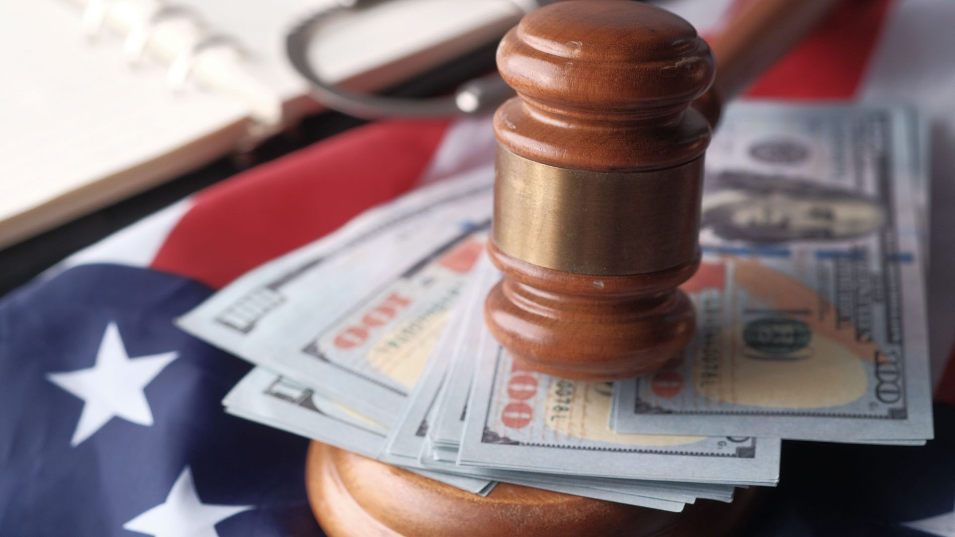 Close-up of a judge's gavel resting on US dollar bills and an American flag, symbolizing justice and finance.