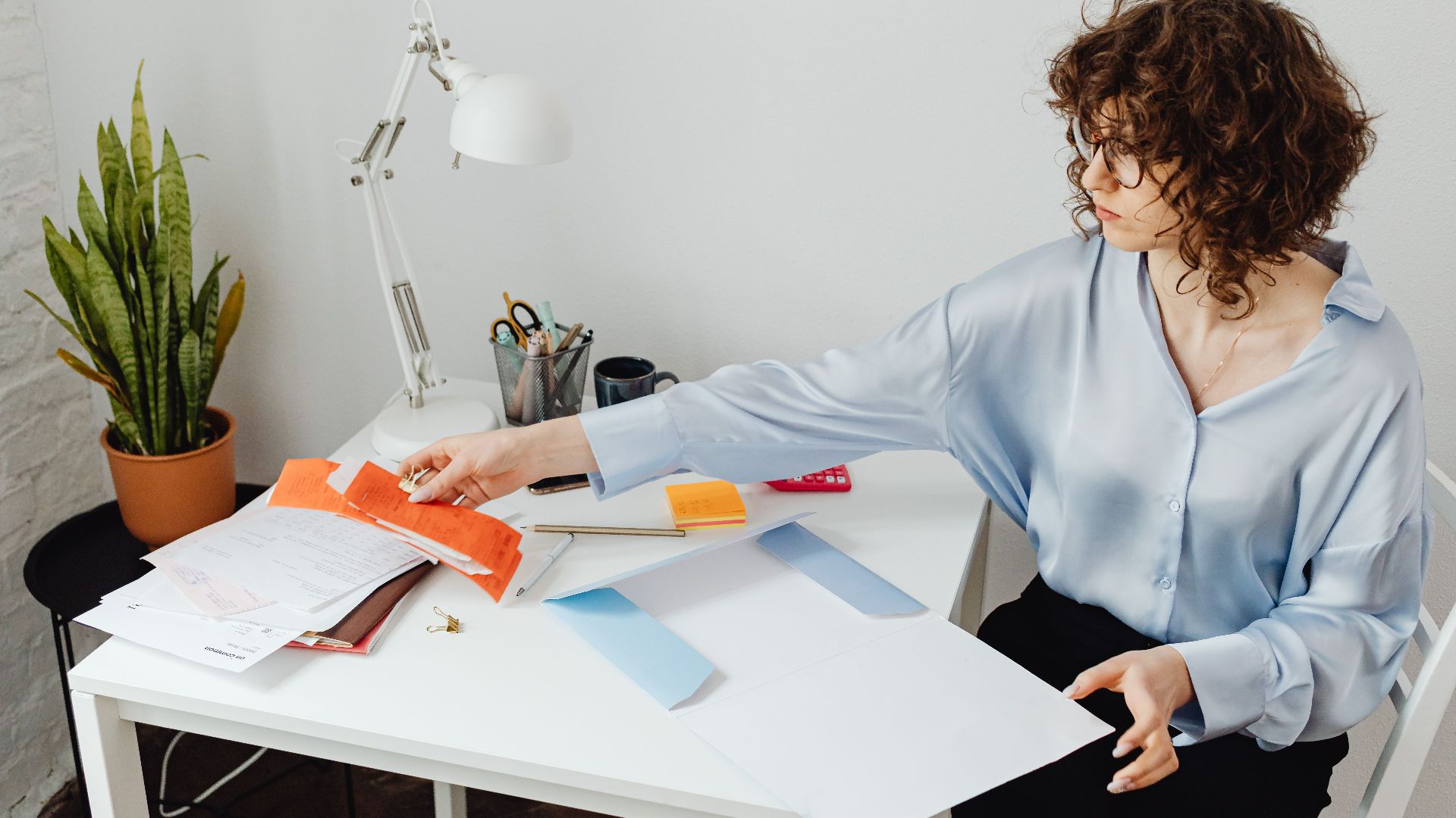 A woman organizing papers at her desk, working in a bright office environment.