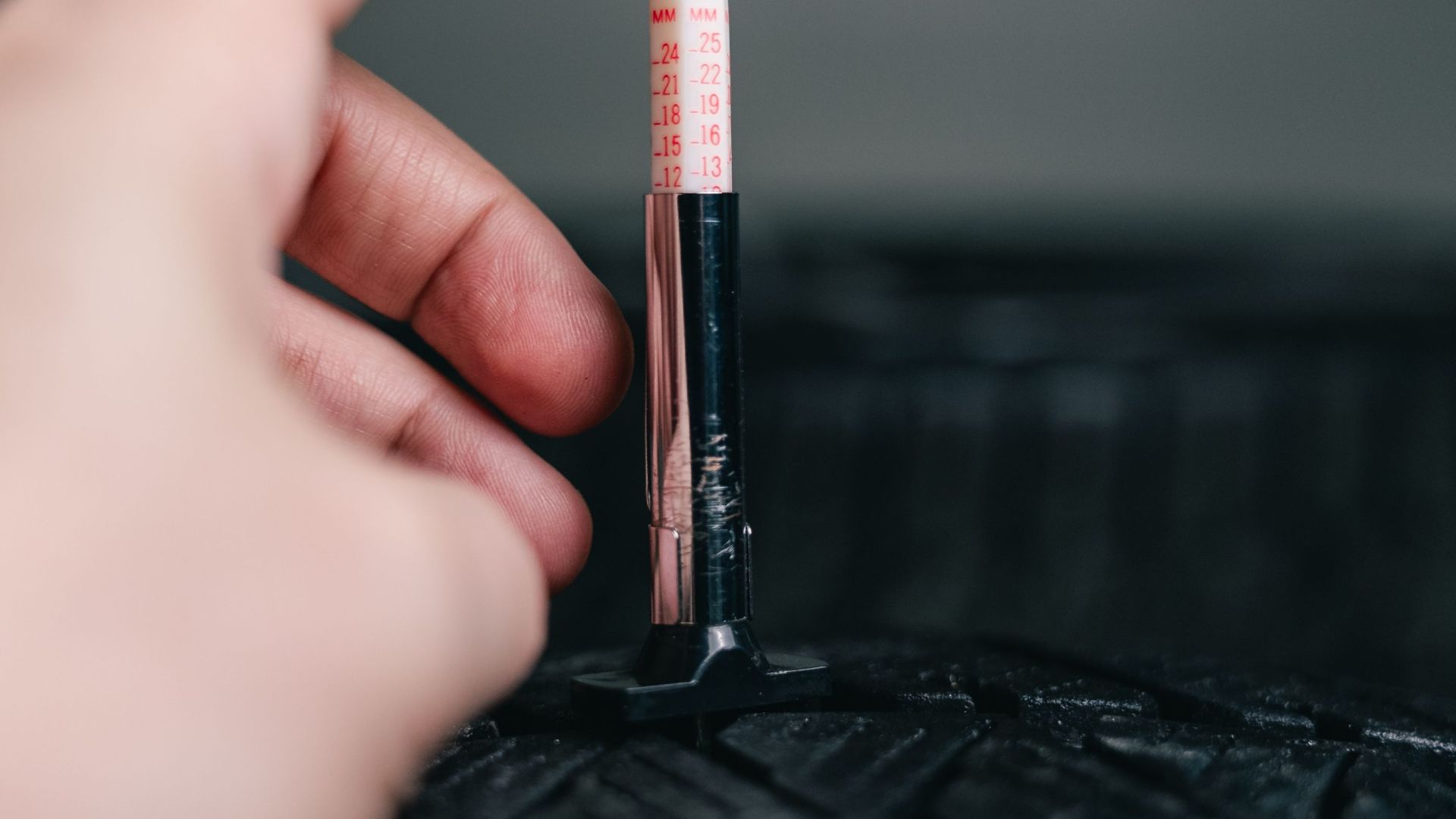 Close-up of hand using a tread depth gauge on a tire. Safety and maintenance check.