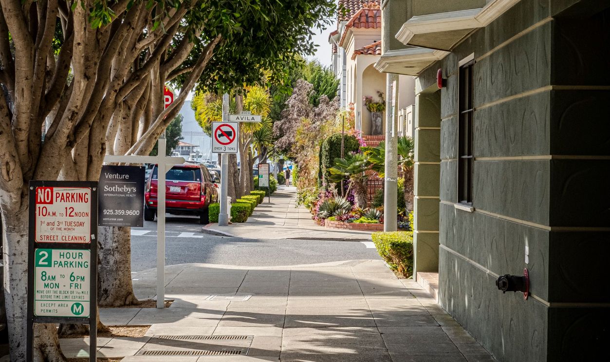 Quiet residential sidewalk lined with trees and buildings on a sunny day