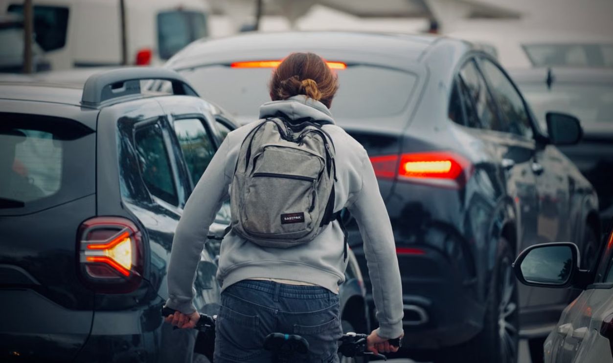 A cyclist wearing a backpack rides through a congested city traffic jam during daytime