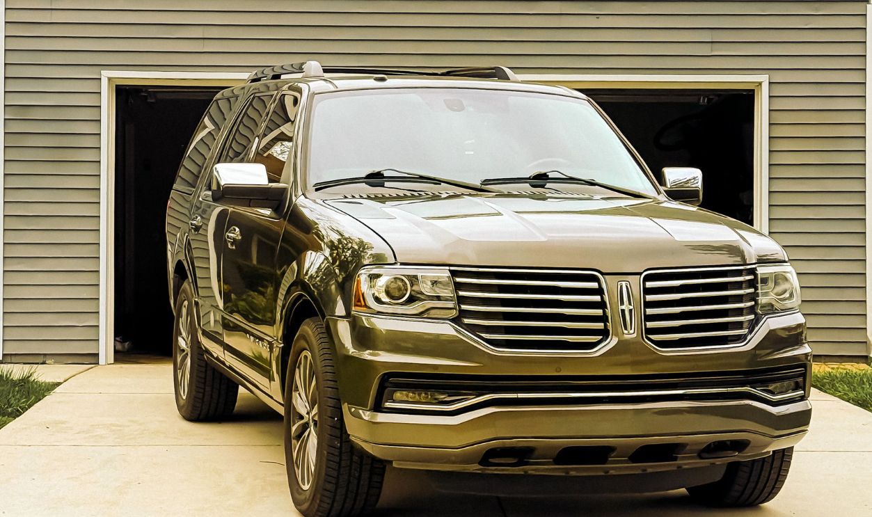 A sleek luxury SUV parked in front of a residential garage on a driveway.