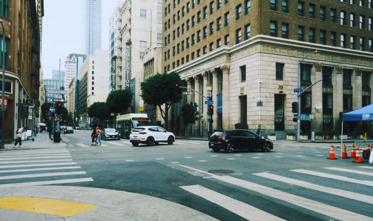 Street view of a busy intersection in downtown Los Angeles featuring cars, pedestrians, and urban architecture