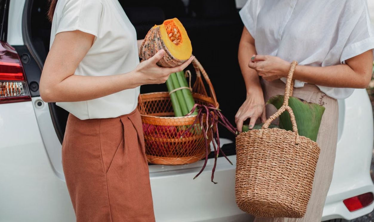Two women unloading organic vegetables from a car into wicker baskets