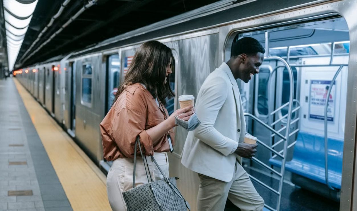 Two adults chatting and entering a train with coffee at a subway station