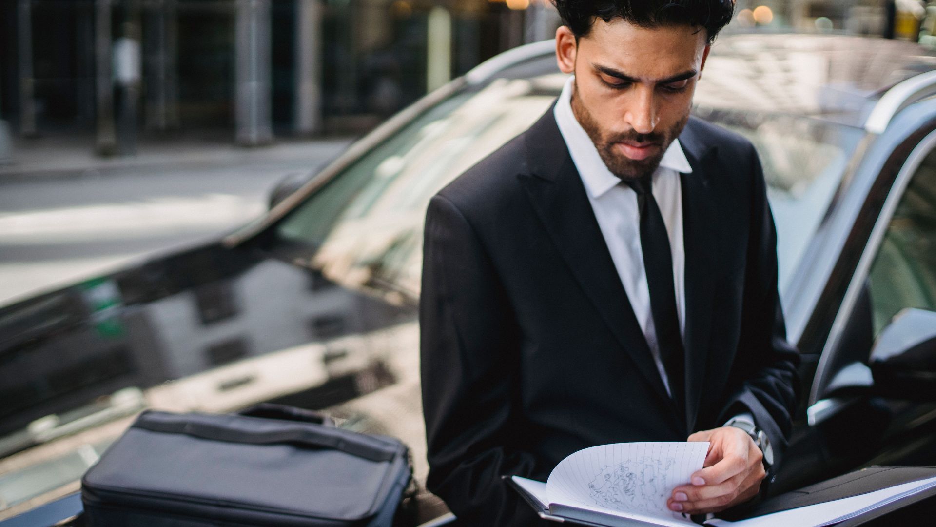 Confident businessman reviewing documents on the street beside a car.