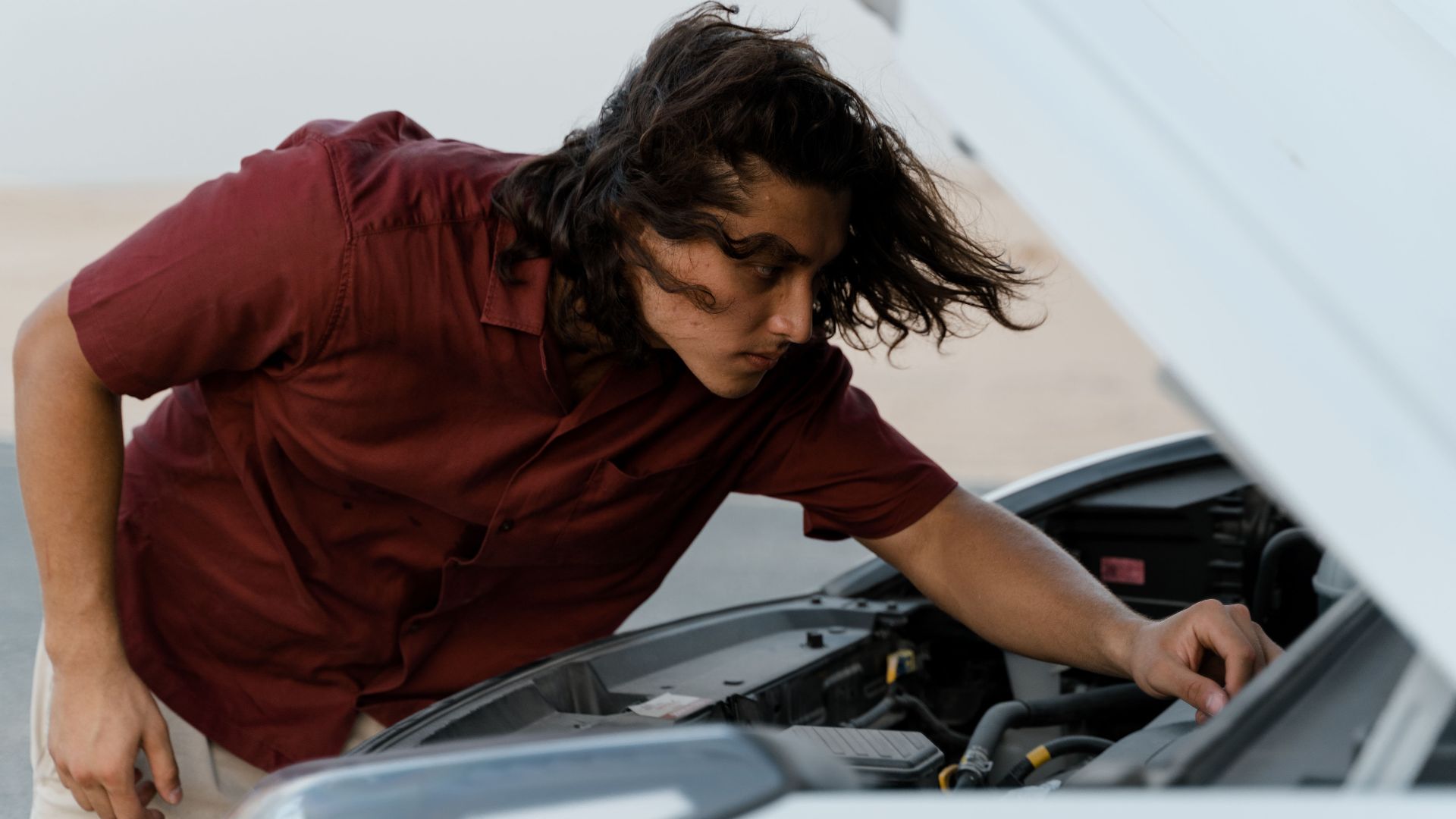 Person checking under the hood of a car for maintenance outdoors on a bright day.