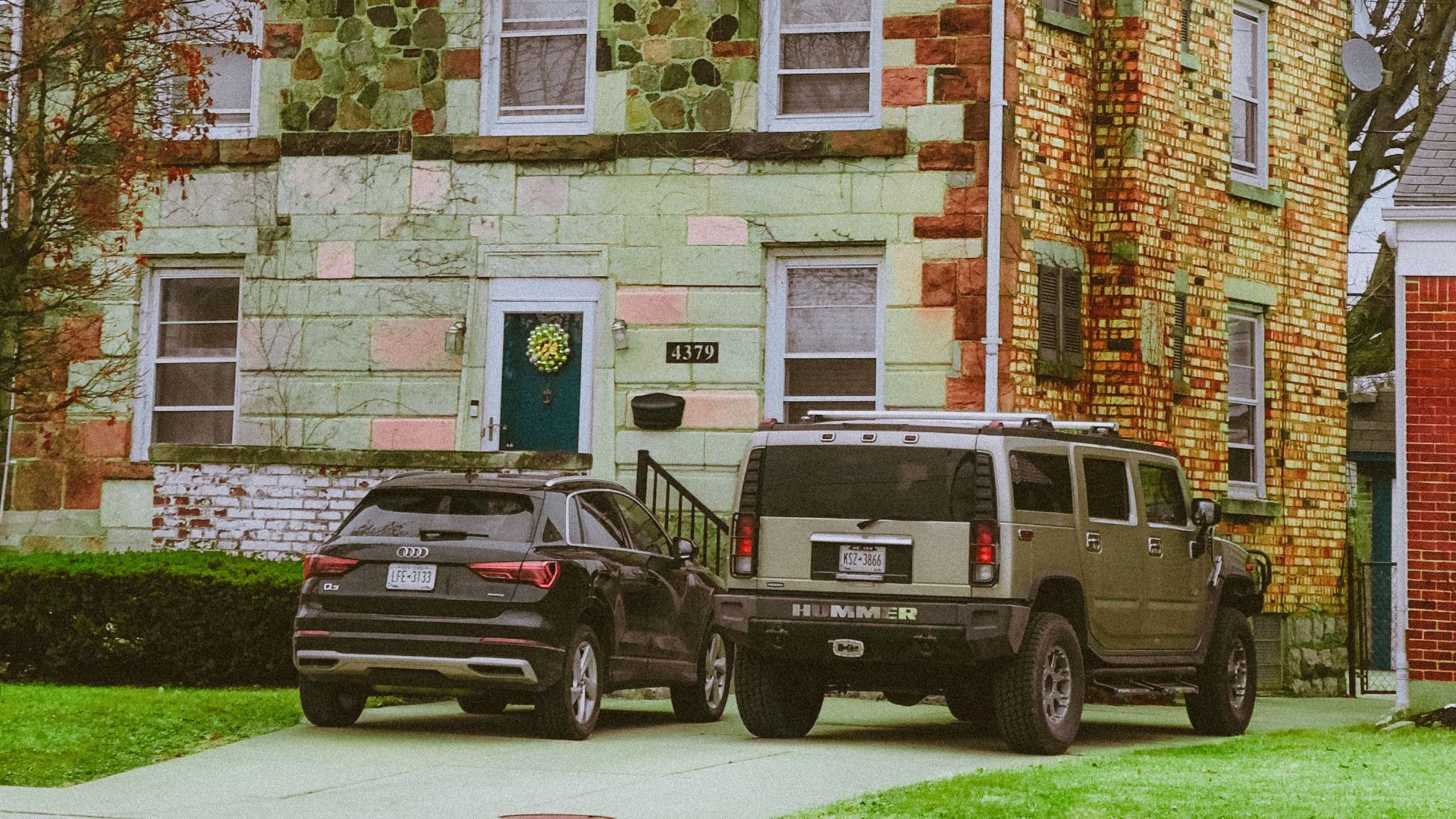 Quaint green brick house with colorful facade and parked cars in suburban setting.