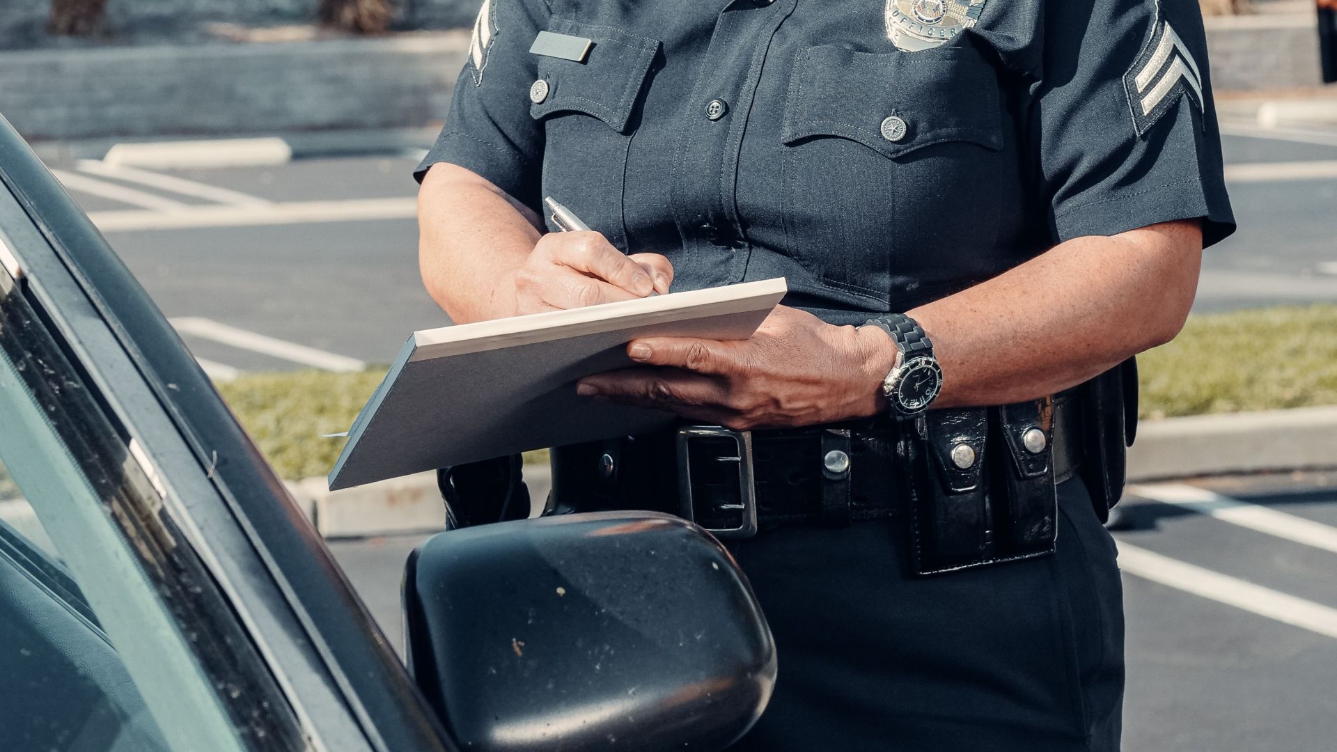 Female police officer writing a traffic ticket in a parking lot.