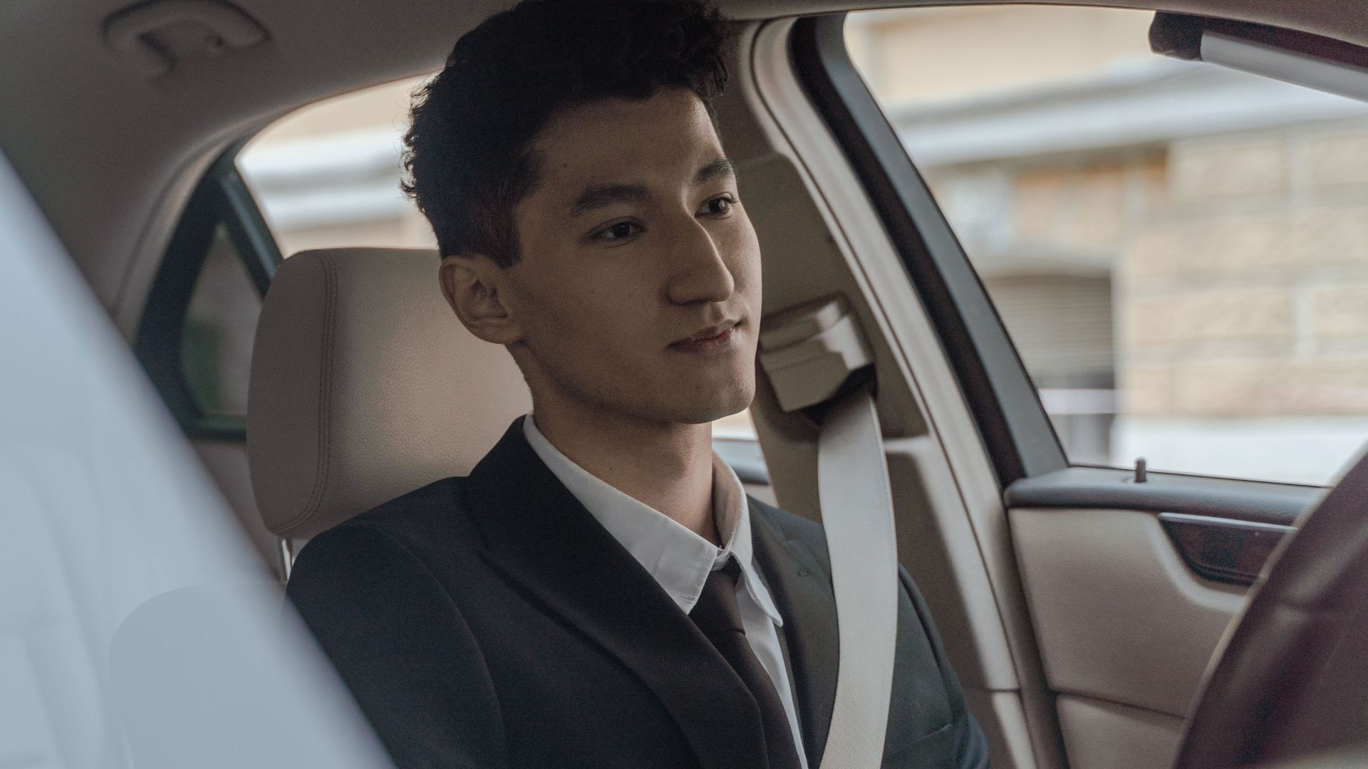 Young professional driver in formalwear inside a modern car, looking focused and attentive.