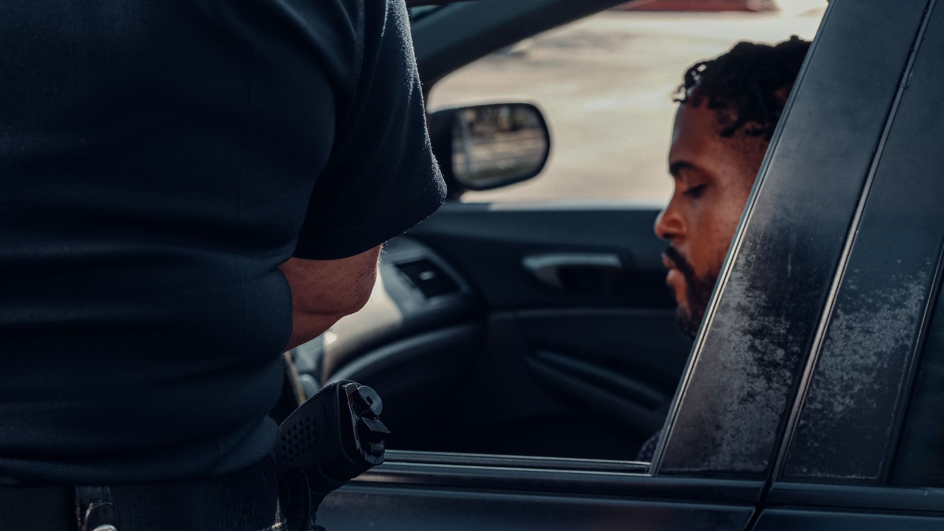 A police officer issuing a ticket to a man seated in a car, captured outdoors in daylight.