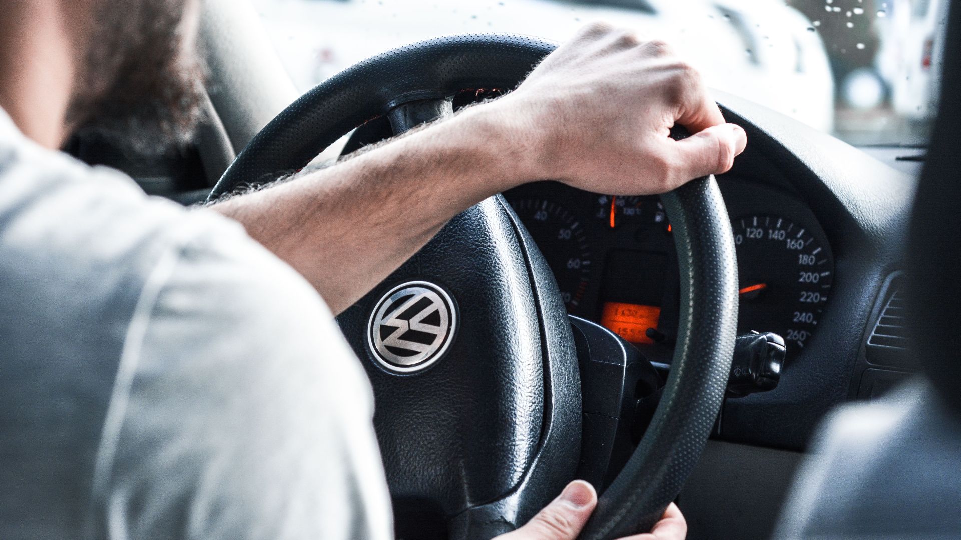 Man gripping Volkswagen steering wheel, focused on driving and vehicle interior details.