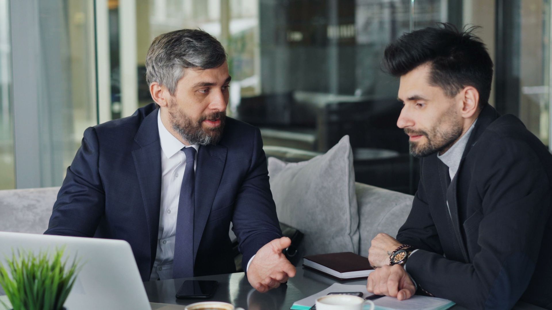 Two businessmen in a café having a professional discussion with coffee and a laptop.