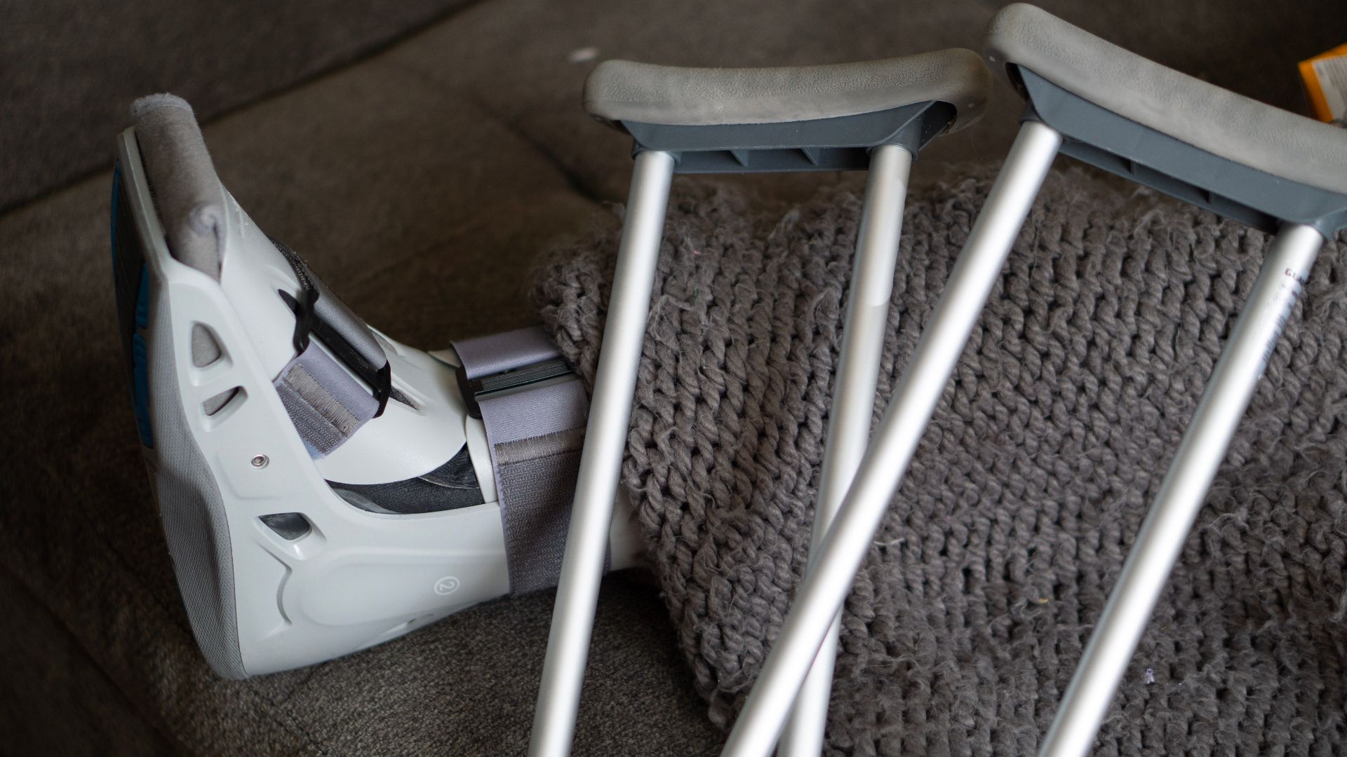 Close-up of an orthopedic boot and crutches on a couch, symbolizing injury recovery at home.