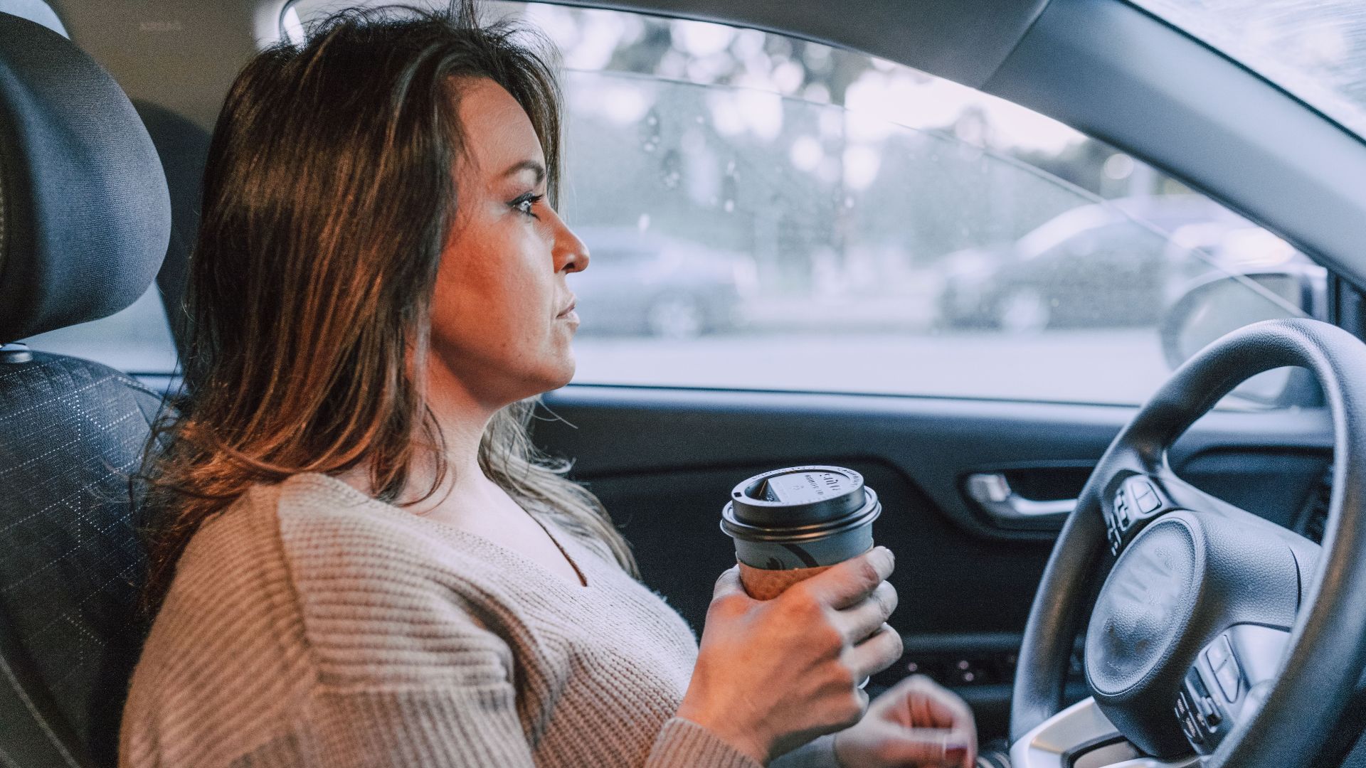 A woman in a car holding a disposable coffee cup, showing focus.