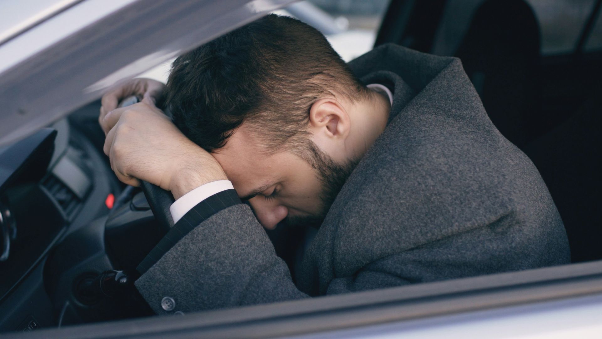 Man resting head on steering wheel in car.
