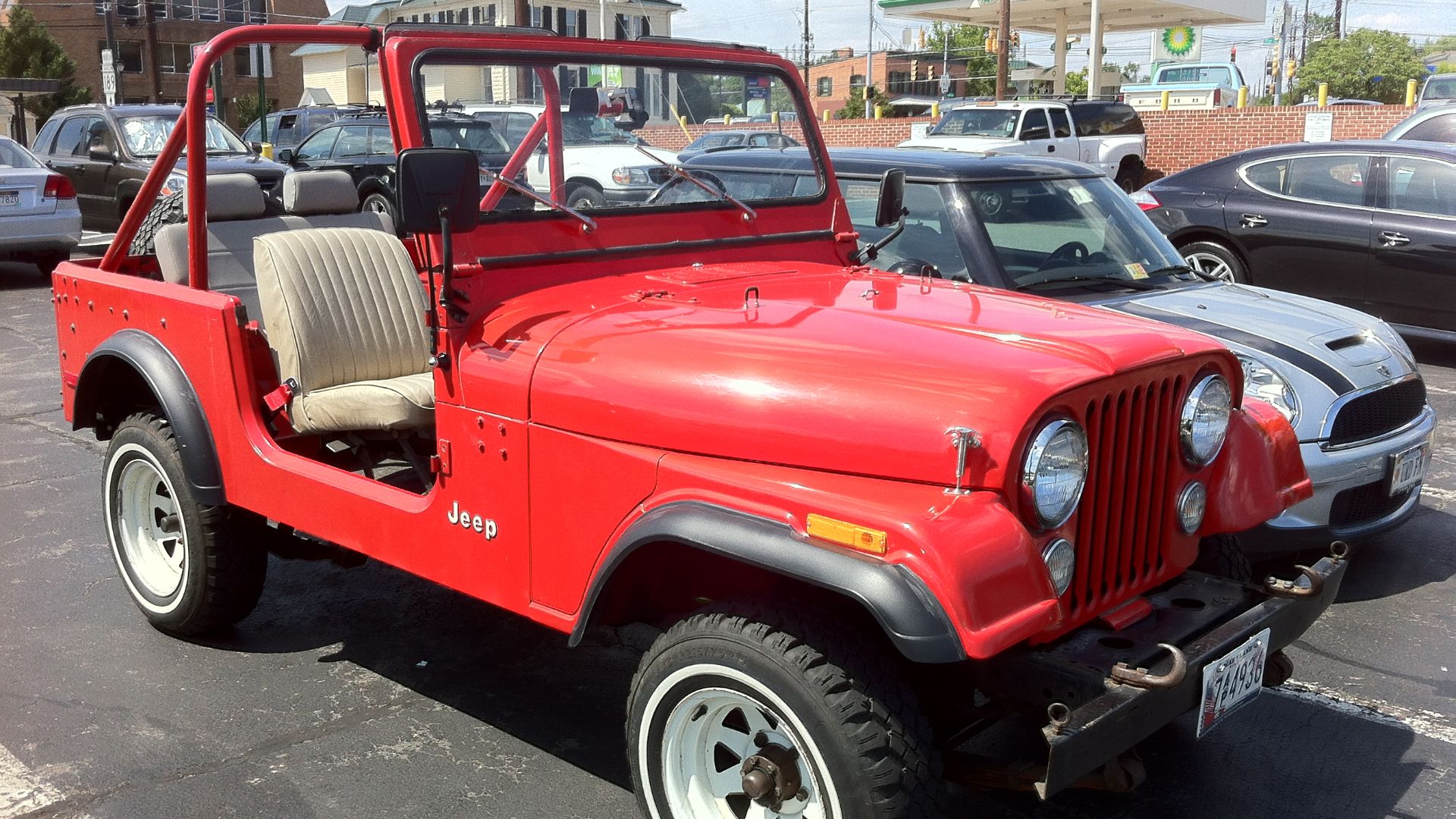 Jeep CJ-7 finished in red, open body with no top. Mostly original vehicle - aftermarket rear seat, but not much customization or extra accessories and components. Front right side view. Photographed in the Village of Potomac, Maryland, USA.