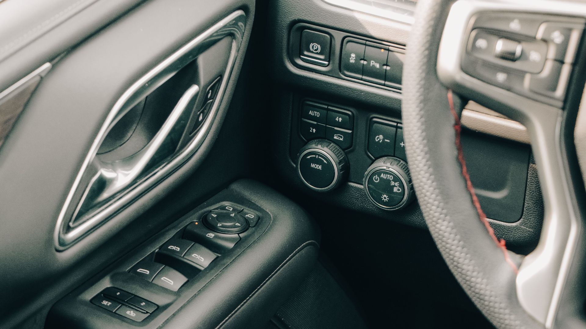 Close-up of a modern car interior showcasing controls, steering wheel, and door handle.
