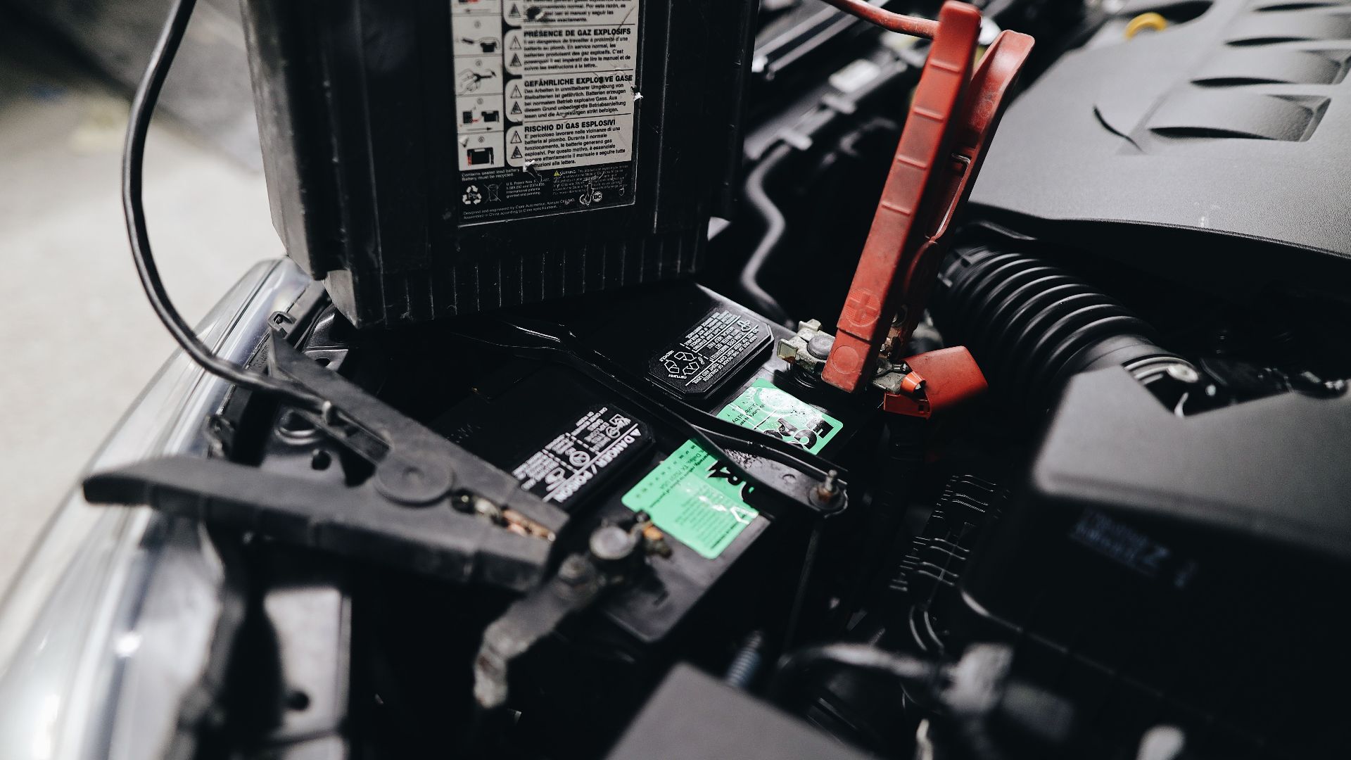 Detailed view of a car battery being jump-started with cables in an engine bay.