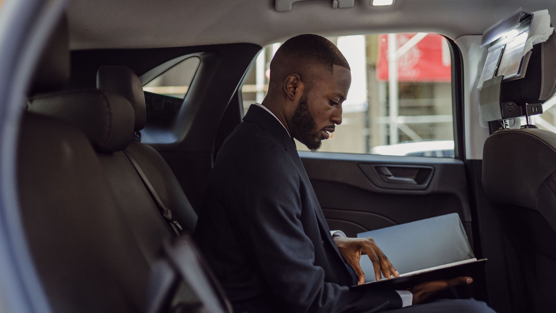 A professional man in a suit reads documents while sitting in a car interior, conveying a business theme.