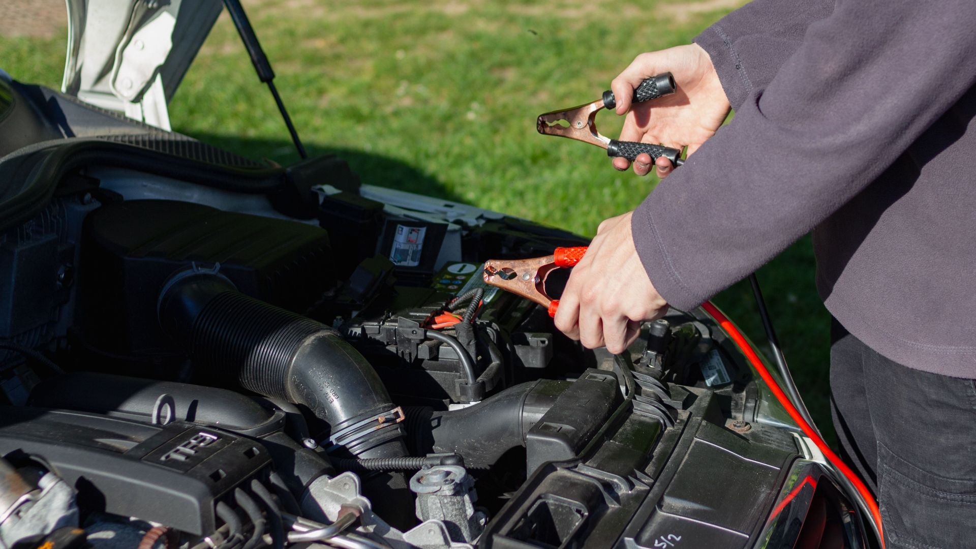 Close-up of mechanic using jumper cables to jump-start a car battery outdoors.