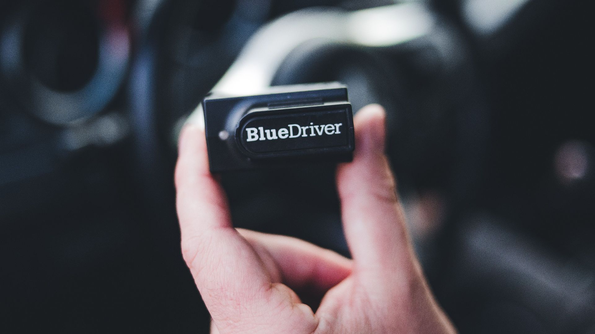Detailed image of a hand holding a Bluedriver OBD2 scanner inside a car.