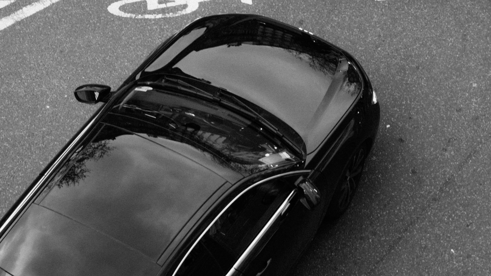 A monochrome image of a black car viewed from above, showcasing its sleek design and reflective surface.