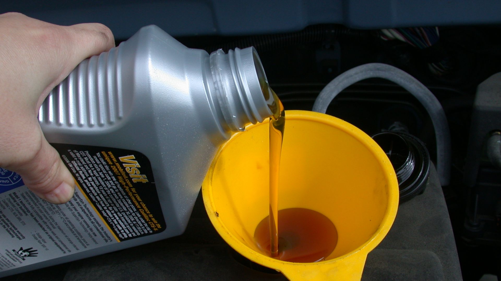 Using a funnel to refill the motor oil in an automobile as part of an oil change.