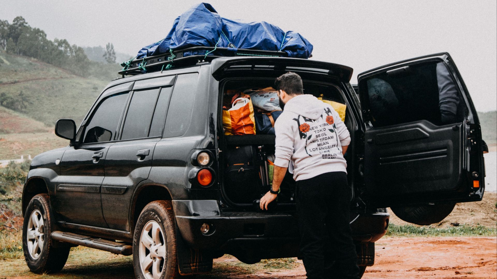 A man packs an SUV with luggage on a dirt road, preparing for an outdoor adventure.