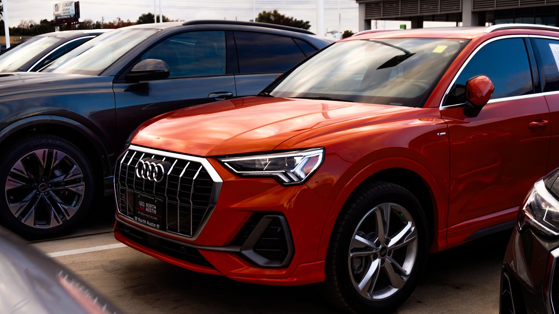 A vibrant orange SUV parked among other vehicles at a car dealership, showcasing modern car design.
