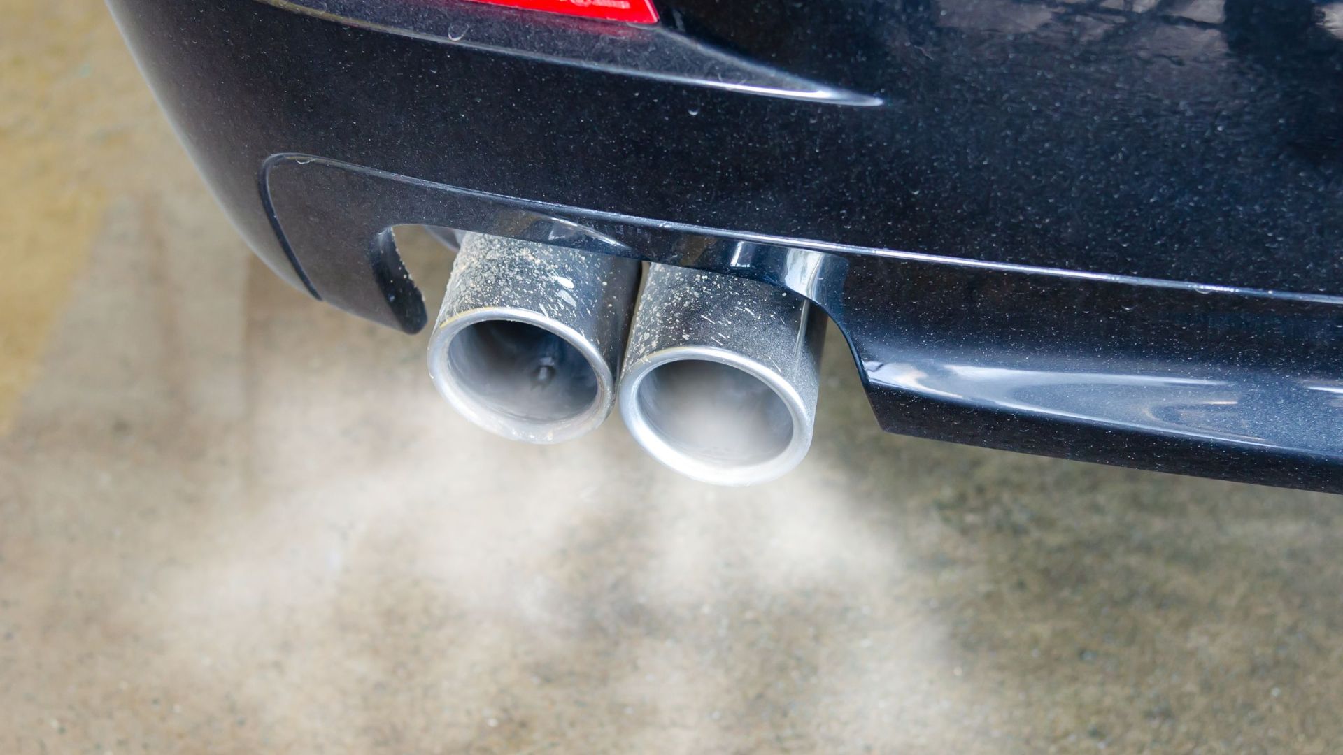Close-up of a car's exhaust pipes emitting visible smoke, highlighting air pollution.