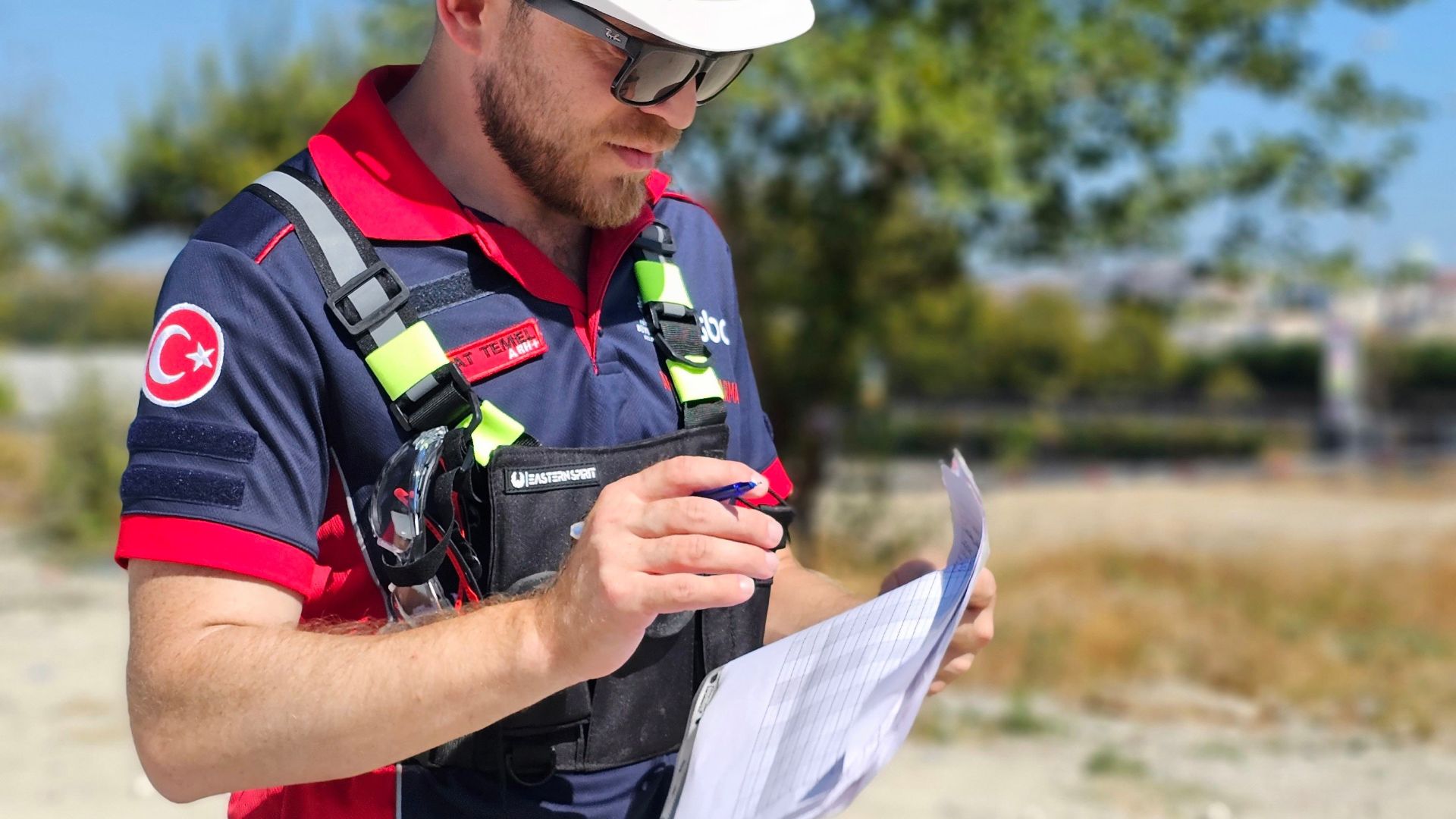 Construction worker in safety gear reviewing documents at a work site on a sunny day.