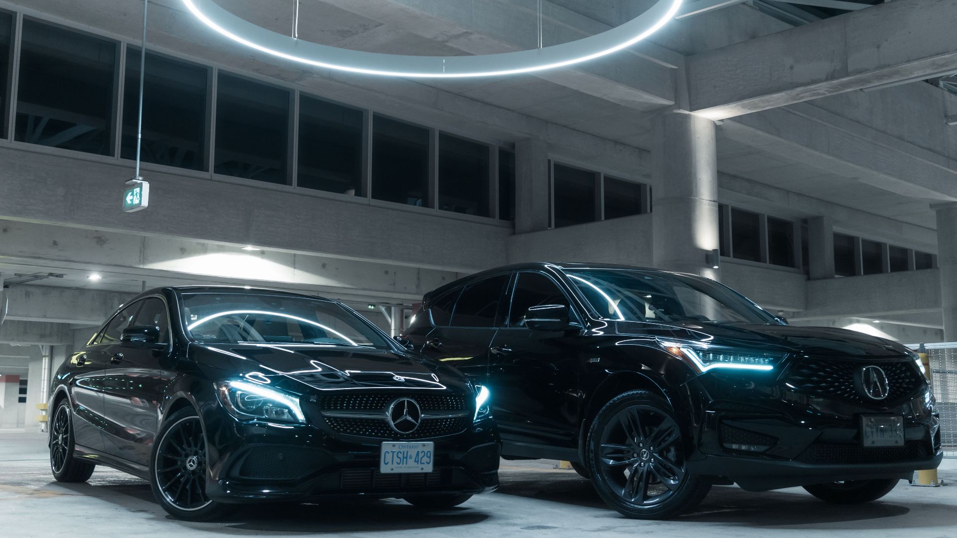 Two luxury cars, a Mercedes and an Acura, parked in an illuminated modern garage.