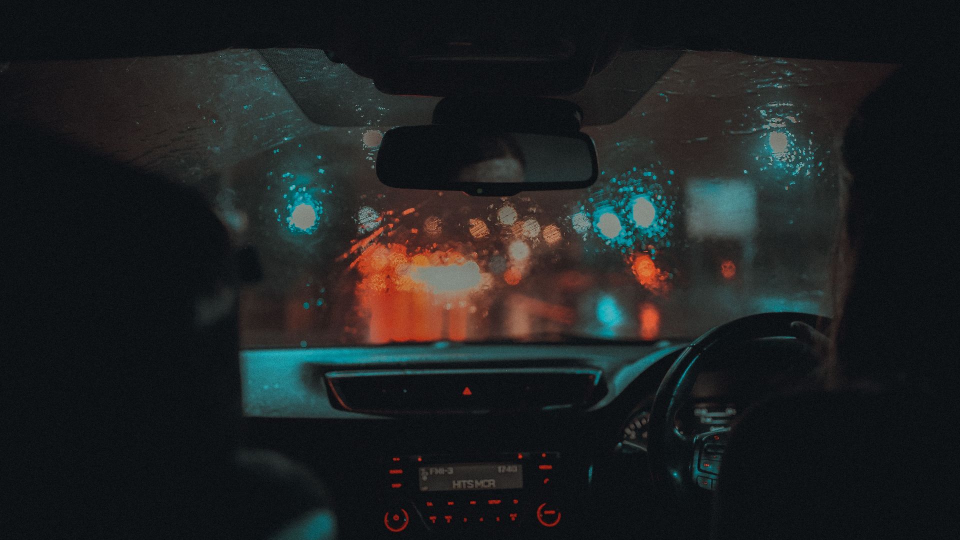 A cinematic view from inside a car driving through rainy Manchester at night with neon lights.