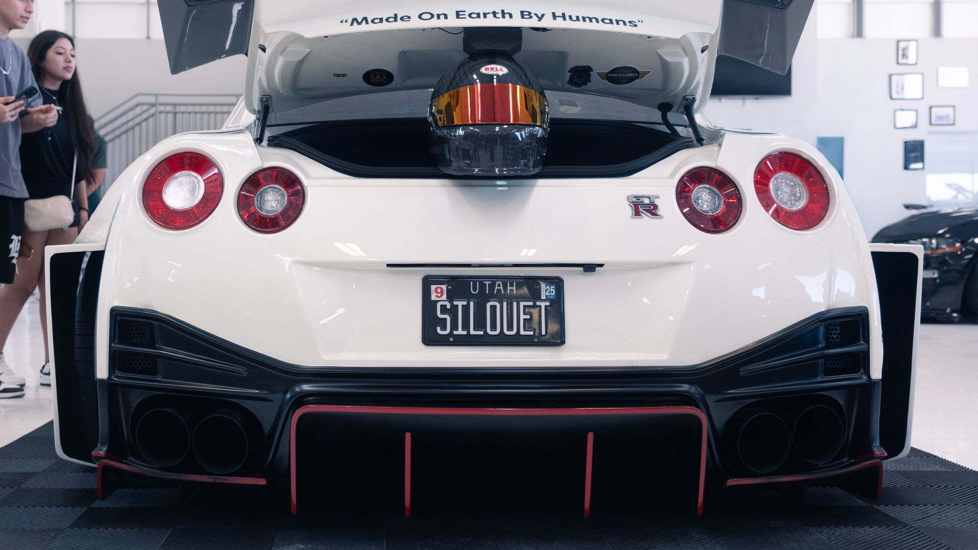 Rear view of a Nissan GT-R with a unique license plate and helmet in the trunk, indoors.