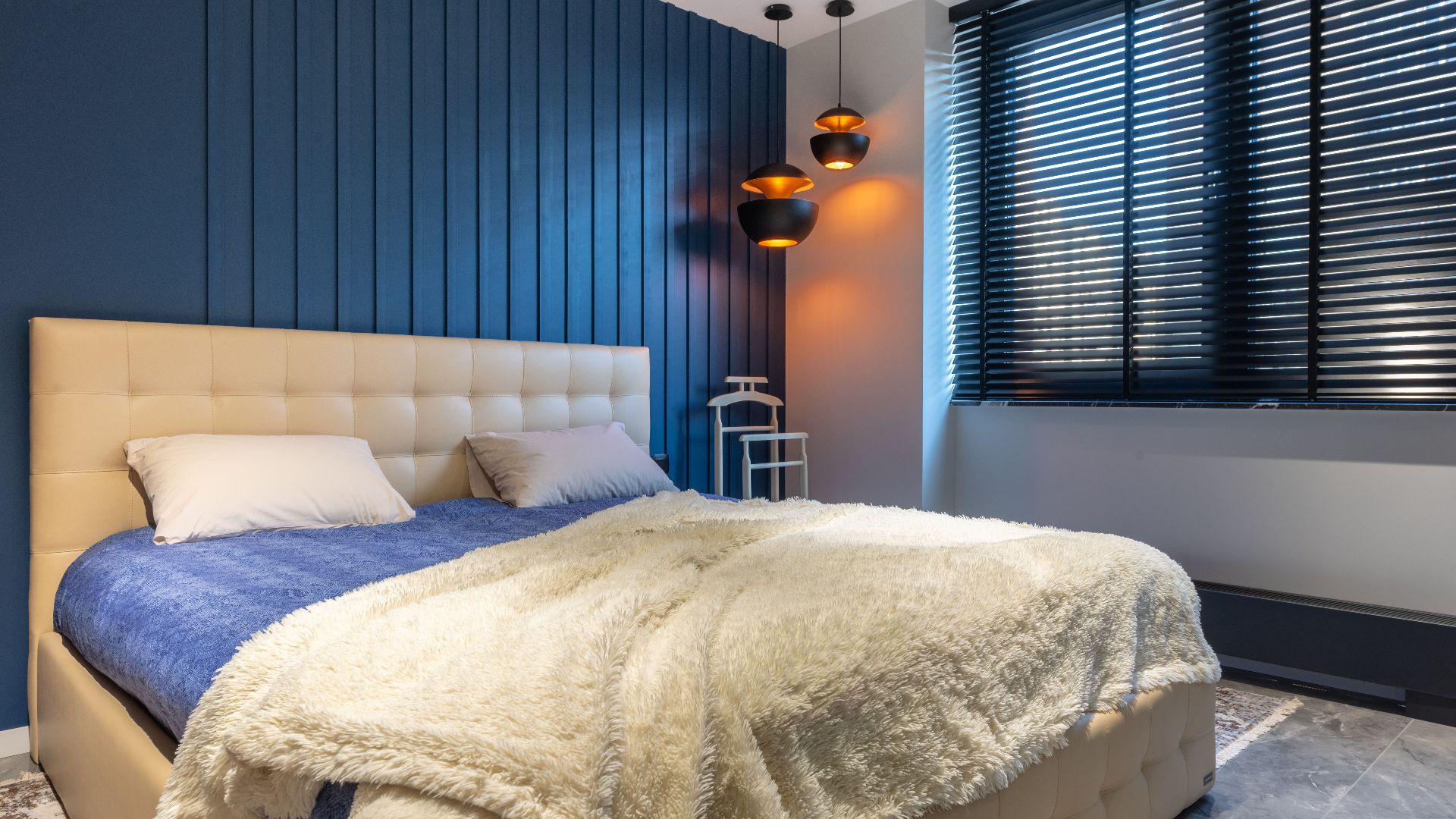 Modern bedroom interior with blanket and pillows on bed against lamps and jalousie in house
