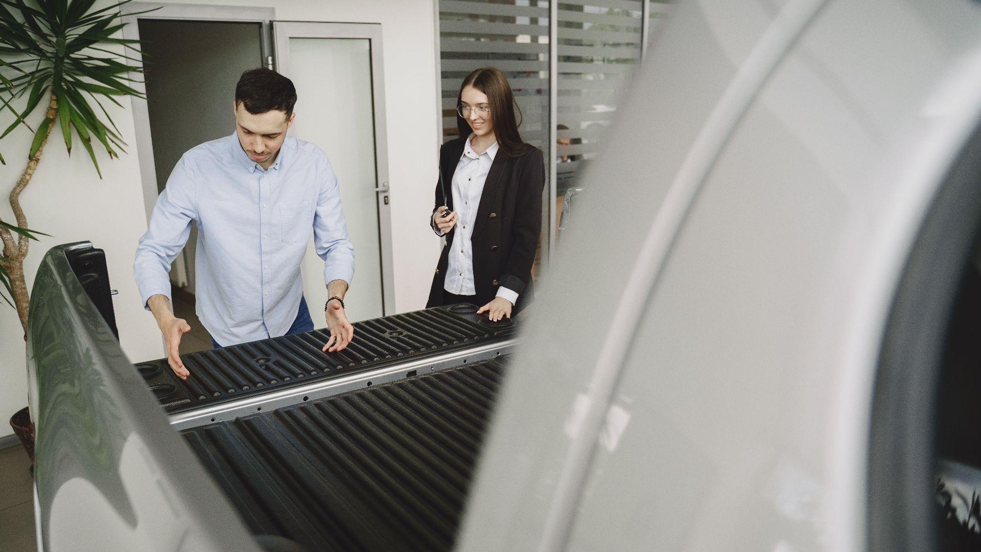 Salesman and client inspecting a pickup truck in a car dealership, discussing features.