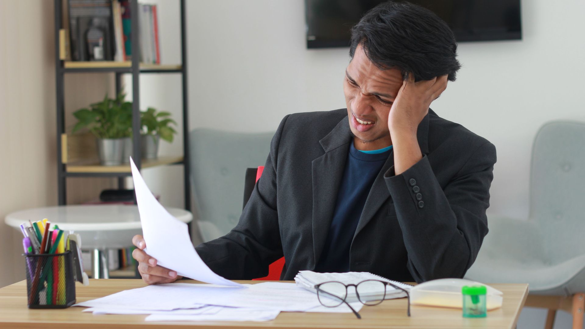 A businessman in an office experiencing stress while reviewing documents.