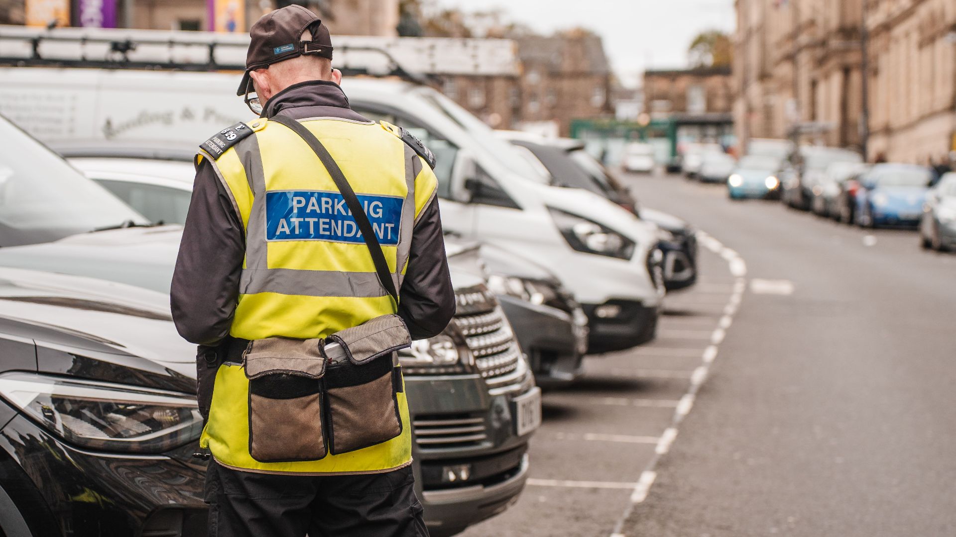 A parking attendant checks cars on a classic Edinburgh street, enhancing urban life.