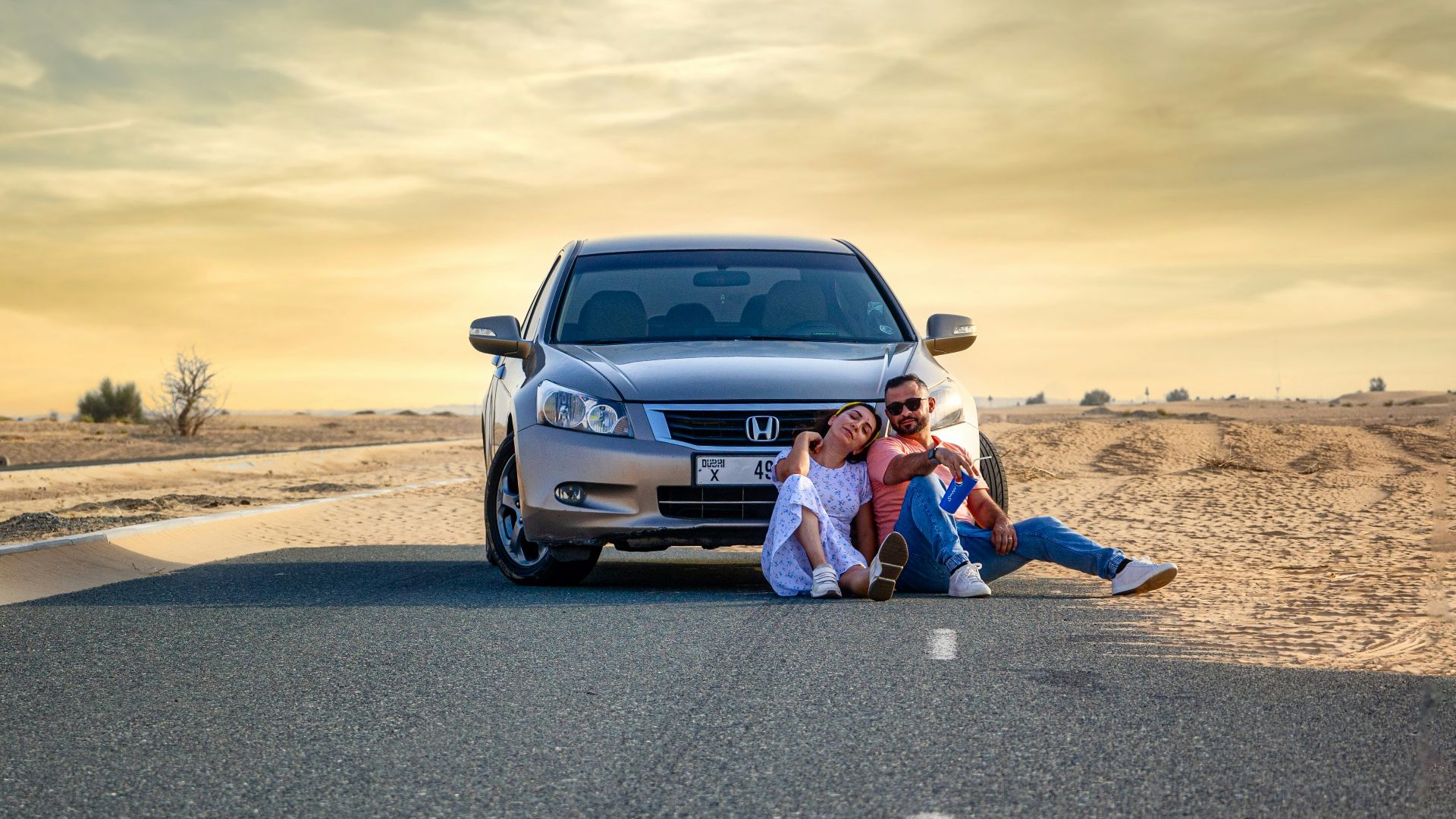 a couple of people sitting on the side of a road next to a car