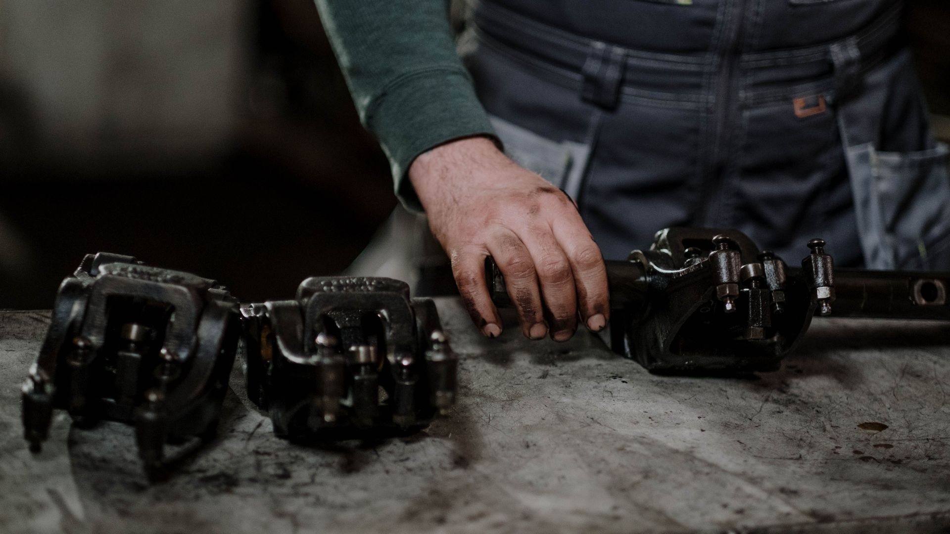 Mechanic in workshop handling greasy metal parts on workbench, depicting repair process.