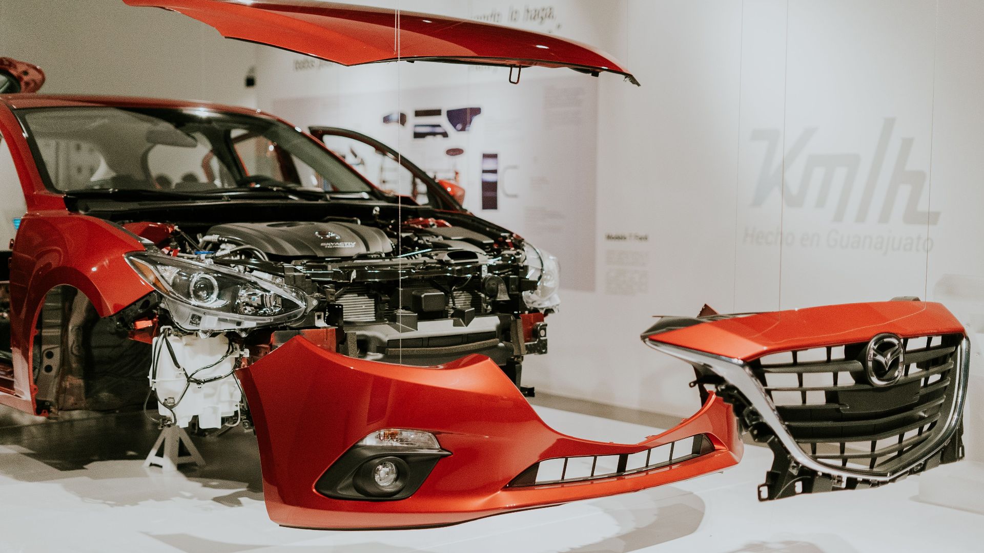 Explore a detailed view of a partially disassembled red Mazda 3 showcased at an auto exhibition.