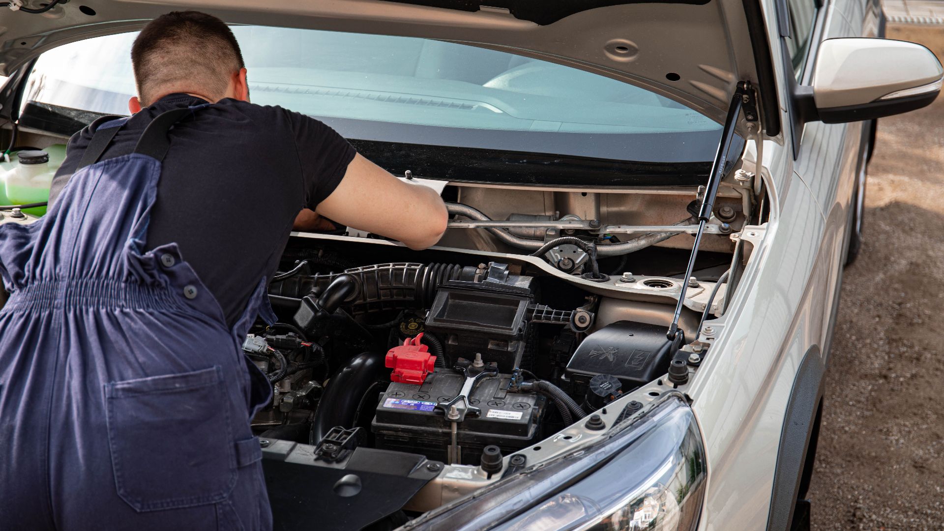 A mechanic fixes a car engine outdoors, focusing on vehicle maintenance.