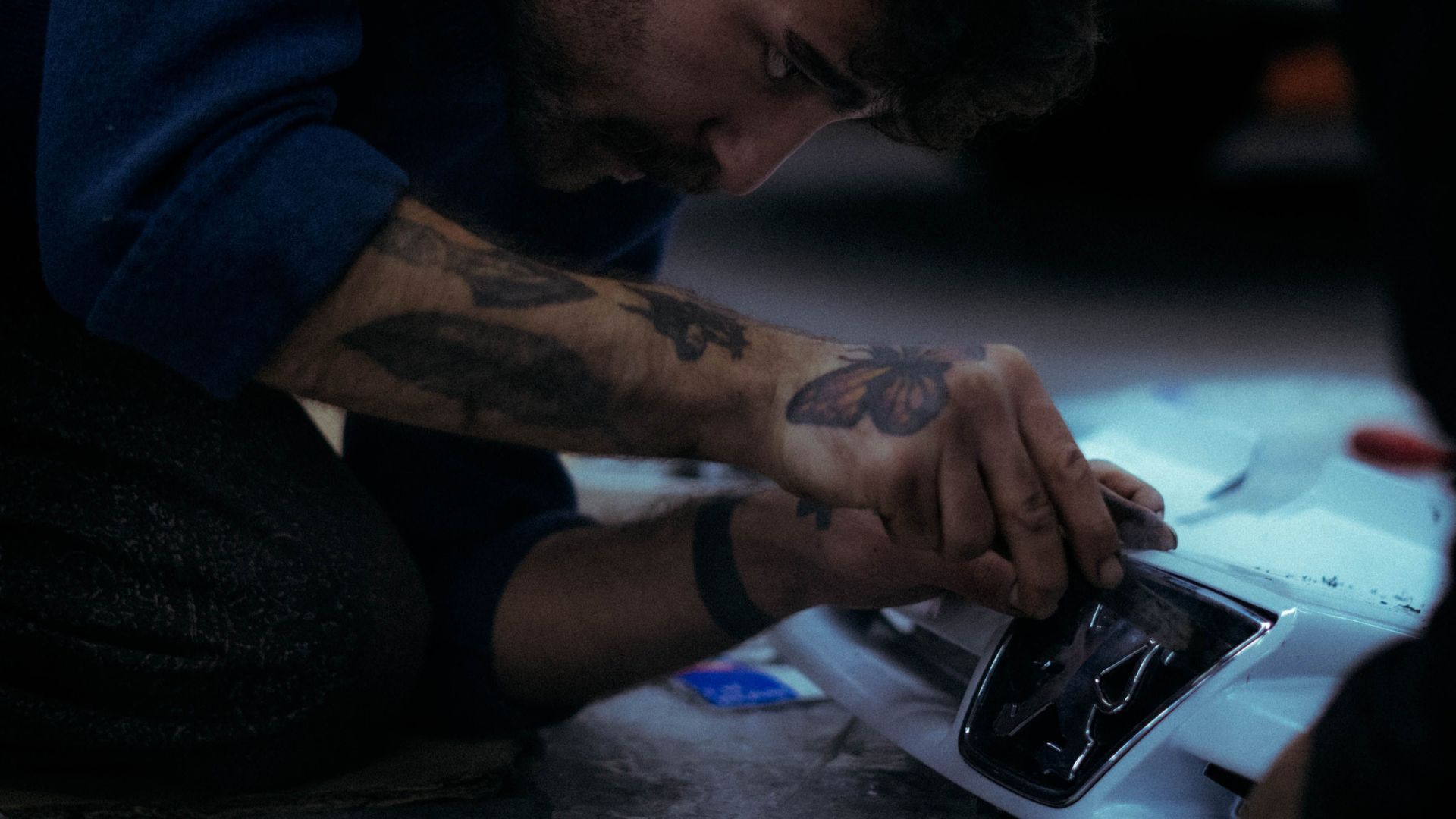 Mechanic intently working on car bumper, showcasing hands-on repair skills.