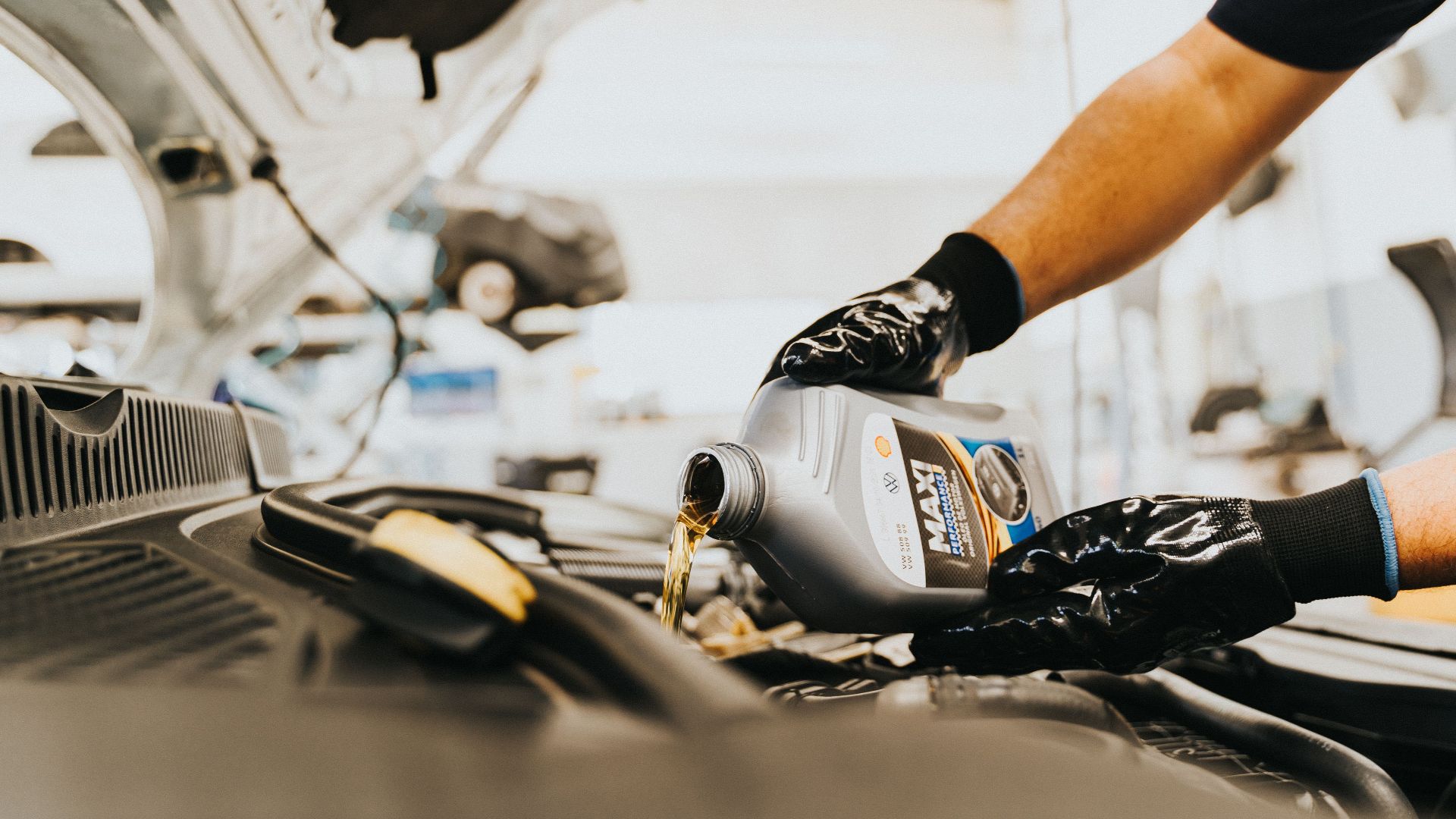 Close-up of a mechanic pouring engine oil in a car inside a garage. Hands wearing gloves.