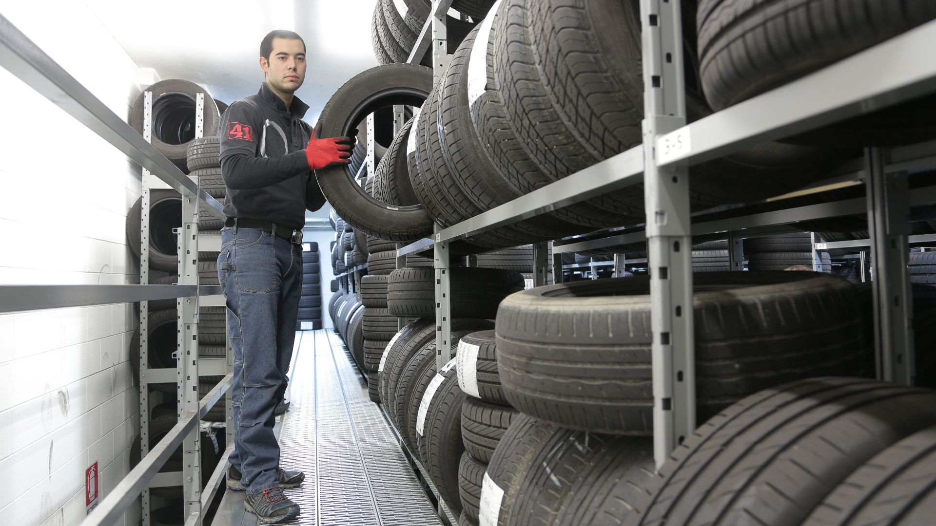 Mechanic places a tire on a rack in an indoor warehouse storage facility.