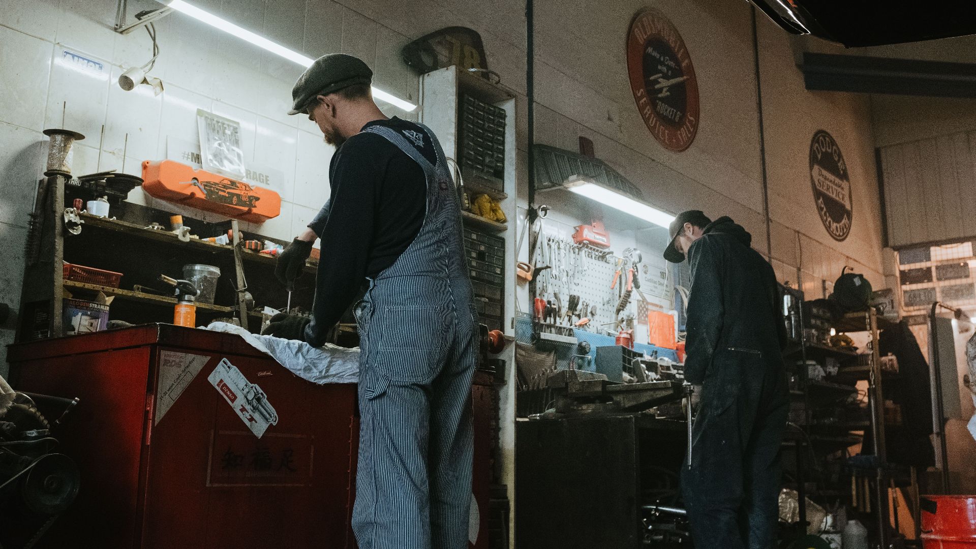 Two mechanics in a garage working on vehicle repair and maintenance.
